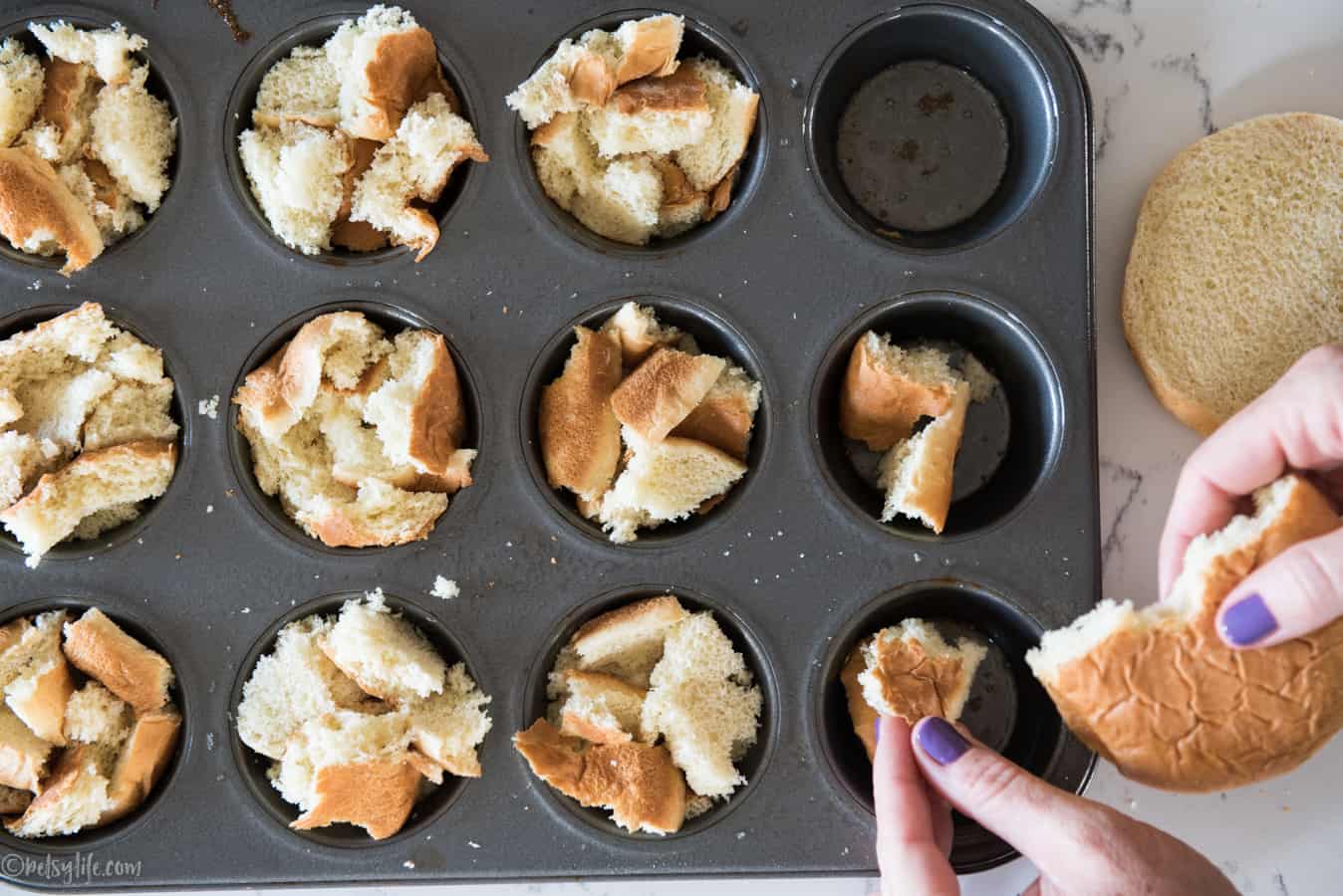 muffin tin being stuffed with torn bits of hamburger buns