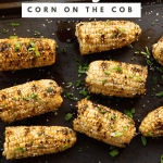 Grilled corn on the cob on a baking sheet garnished with sesame seeds and green herbs