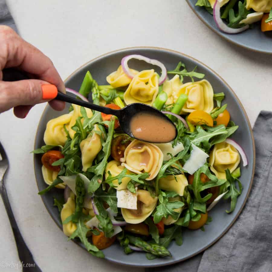 Spoon drizzling dressing over a plate of warm tortellini salad 