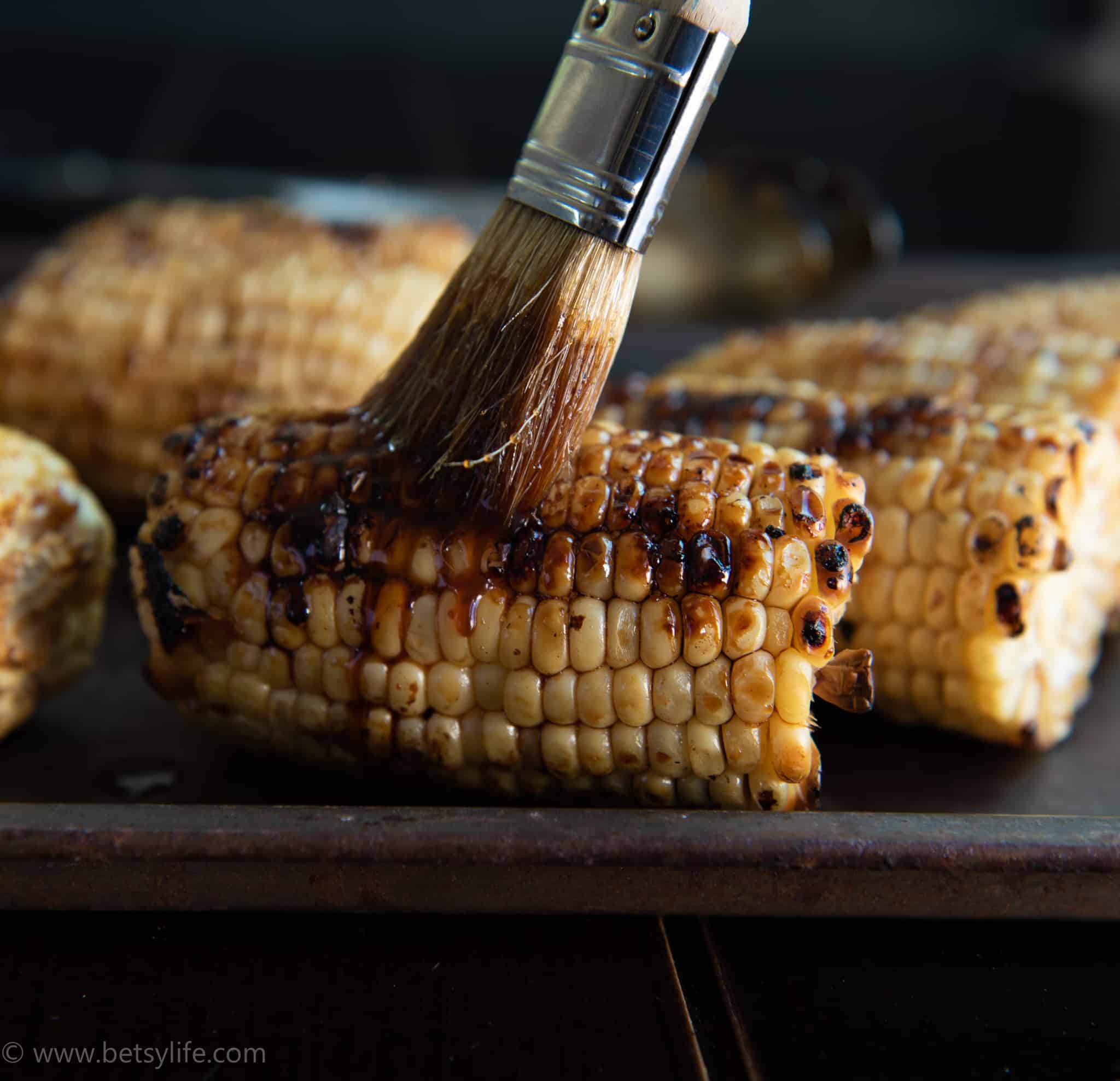 grilled corn on the cob being brushed with sauce