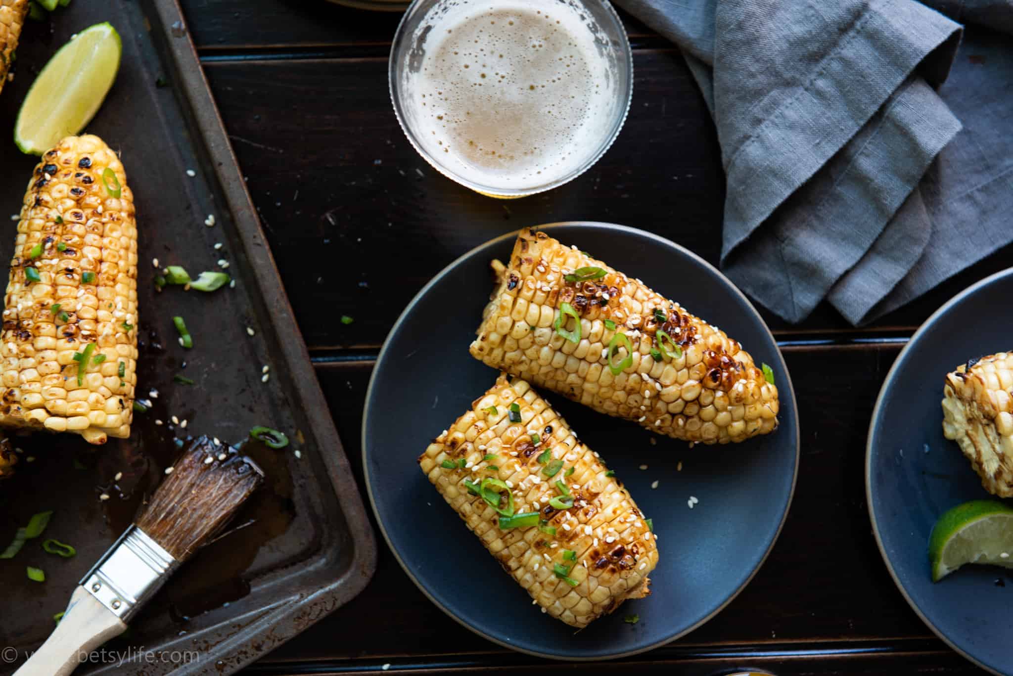 Plate of sesame glazed corn on the cob with two servings next to a beer 