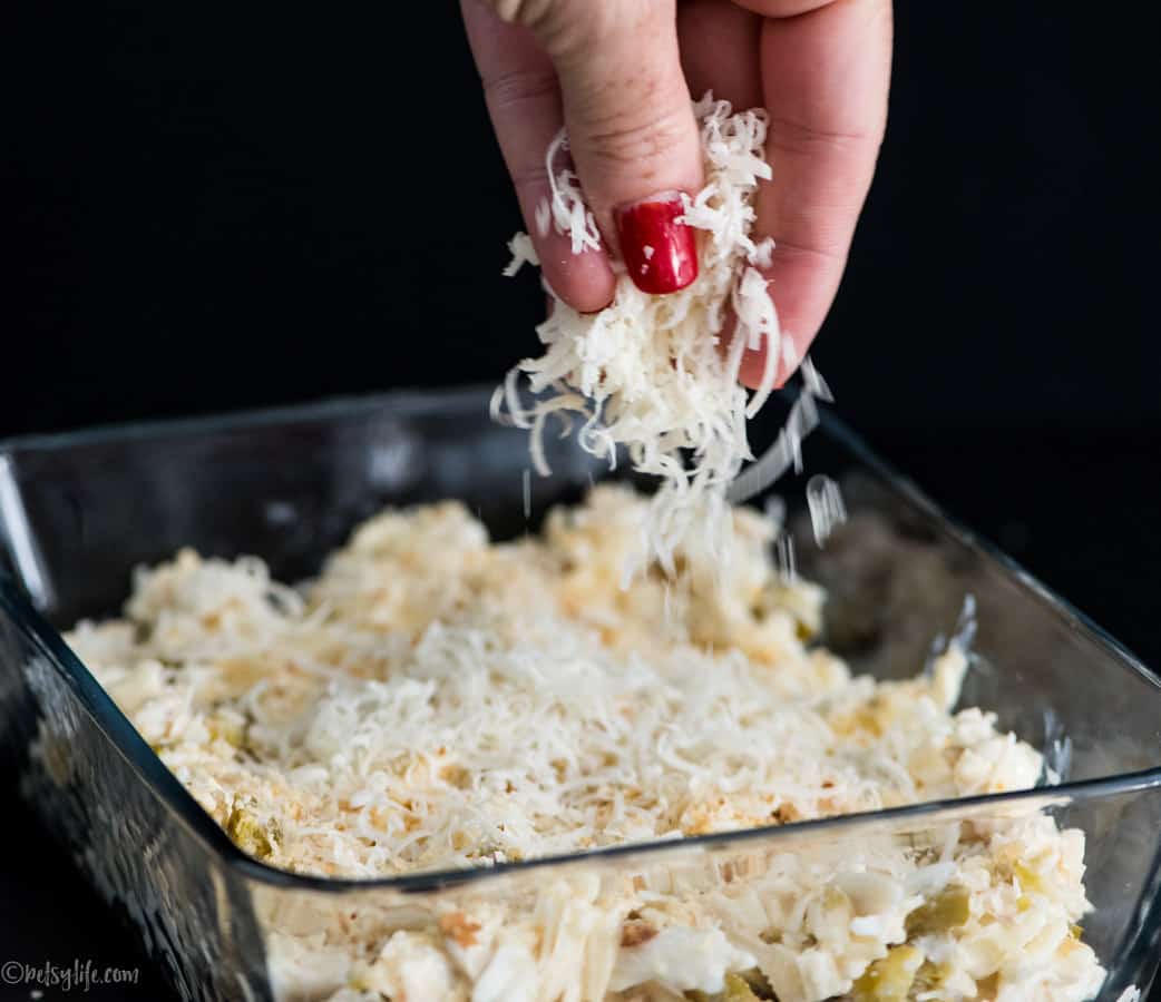 hand sprinkling cheese over jalapeno crab dip in a baking dish 