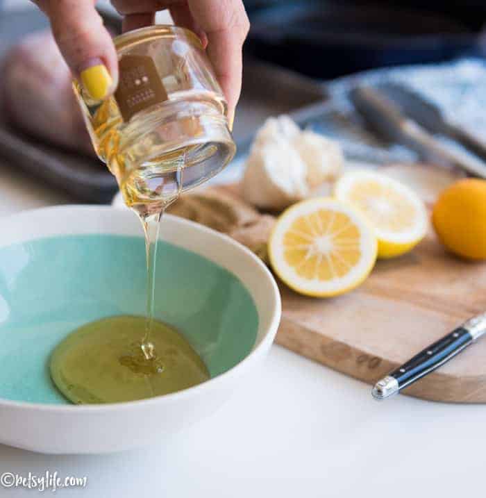small jar of honey being poured into a teal bowl with lemons on a cutting board in background