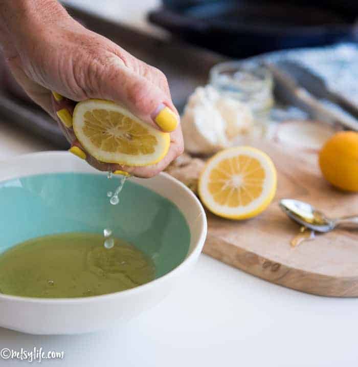 half lemon being squeezed into a teal bowl with a cutting board in background