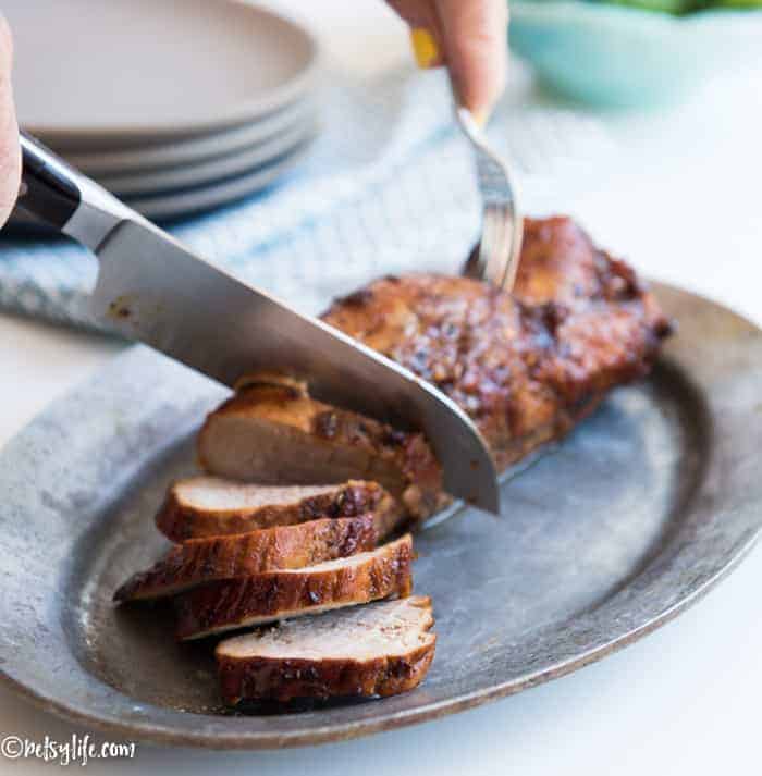 simple honey bbq pork tenderloin being sliced with a black handled knife on a metal serving plate