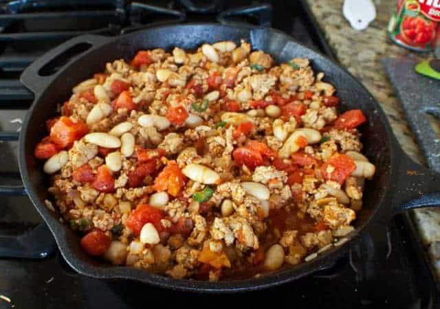 beans, tomatoes and ground turkey cooking in a cast iron skillet