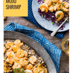 gray plate with a serving of orange shrimp, quinoa and cabbage next to a metal serving dish with the same ingredients. Two glasses of white wine and two blue napkins