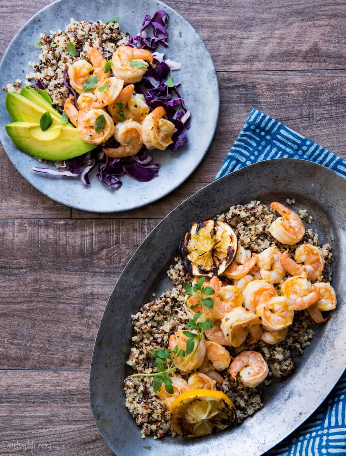 Metal serving plate full of orange shrimp and quinoa next to a gray plate of a dished up serving