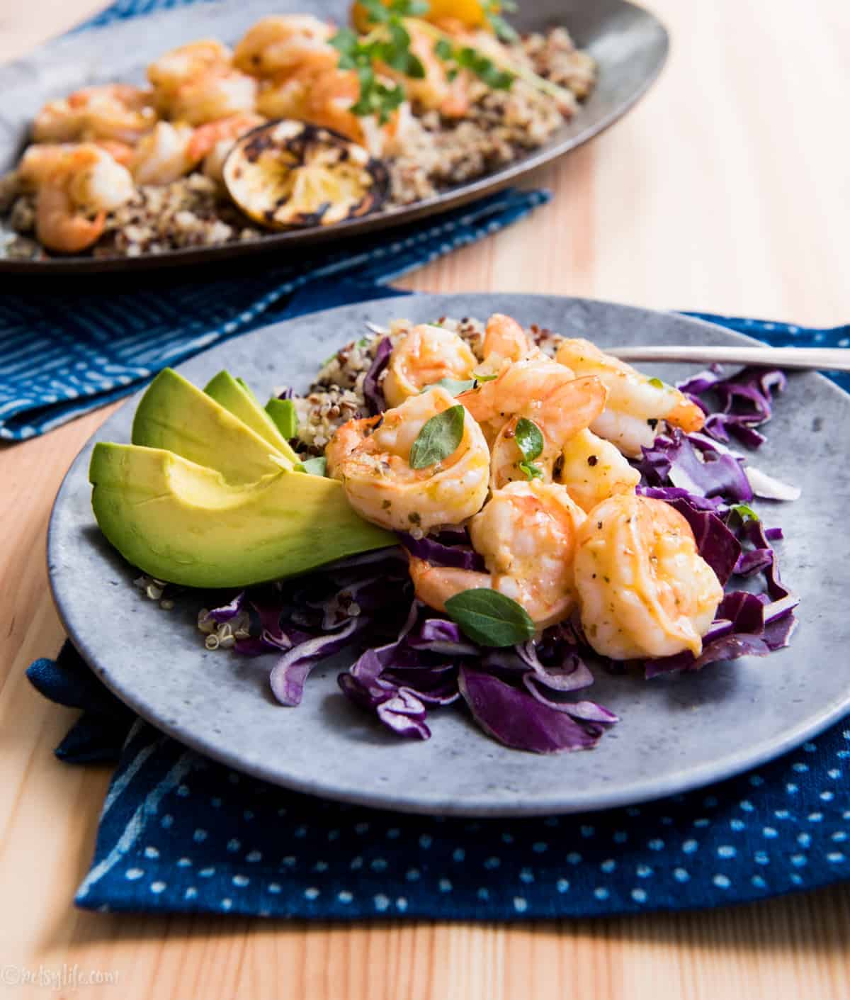 gray plate with a serving of orange shrimp, purple cabbage and avocado on a blue napkin