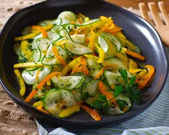 Easy Cucumber Salad. Thinly sliced cucumbers, orange and yellow bell peppers and fresh herbs on a brown oval plate