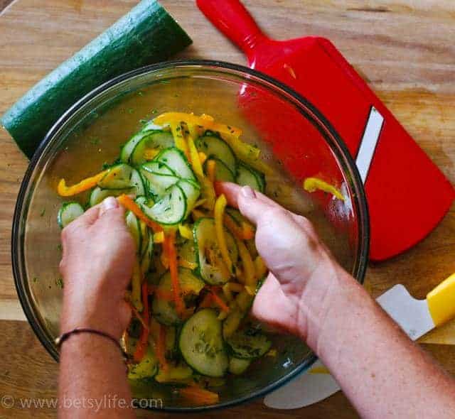 Easy Cucumber Salad being tossed in a clear bowl with two hands 