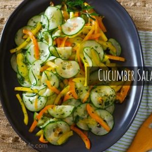 Easy Cucumber Salad. Thinly sliced cucumbers, orange and yellow peppers and fresh herbs on a dark oval serving platter