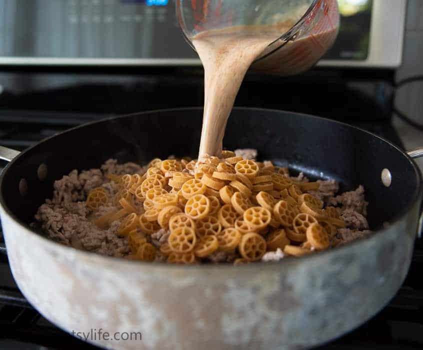 pan of ground turkey and dry pasta with sauce being poured over the top 