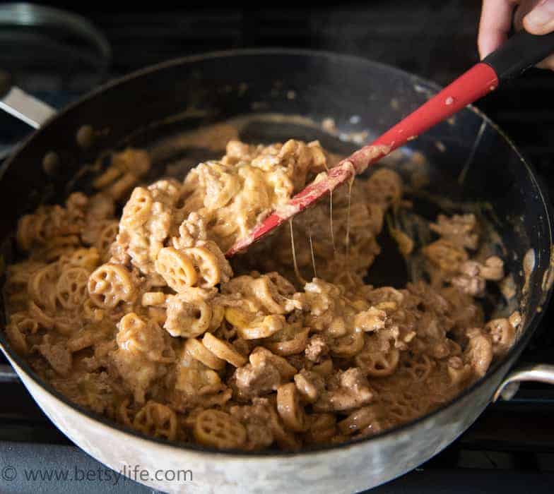 pan of cheesy homemade hamburger helper being stirred with a red spatula 