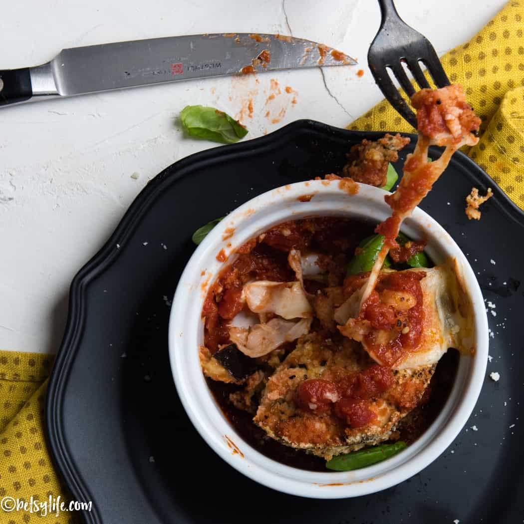 Fork pulling a cheesy bite from an individual eggplant parmesan baked in a ramekin. 