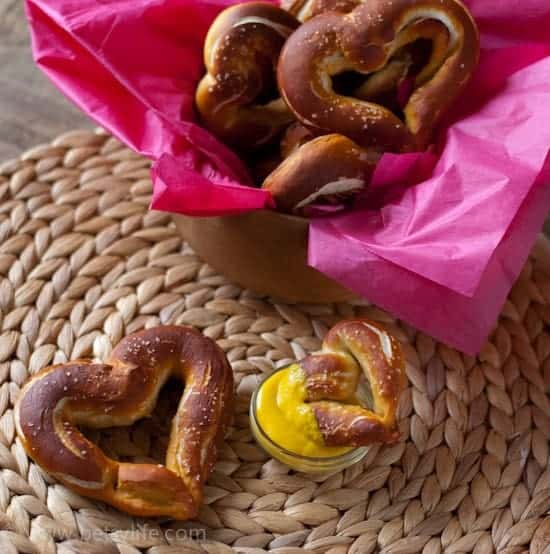 homemade heart shaped pretzels in a basket lined with pink tissue and on a woven mat with a small dish of mustard 