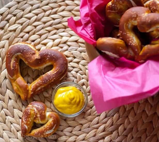 heart shaped homemade pretzels on a woven mat next to a small dish of mustard 