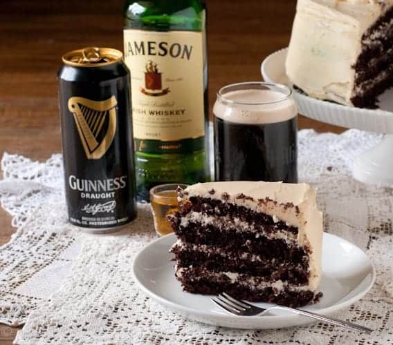 Slice of Boozy Chocolate Stout Cake next to glass of stout beer and a bottle of whiskey