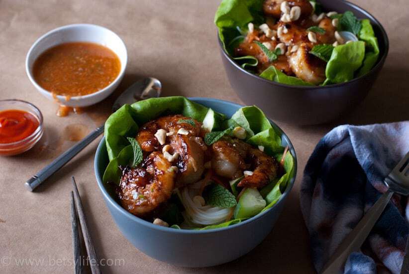Grilled shrimp over greens in a blue bowl with orange sauce in the background