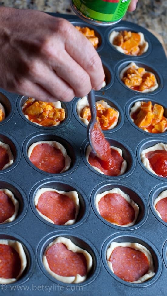hand spooning pizza sauce into a mini muffin pan full of pizza snack bites 