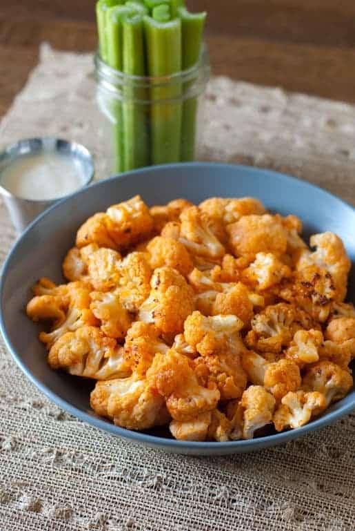 Blue bowl of buffalo cauliflower with a jar full of celery sticks in the background 