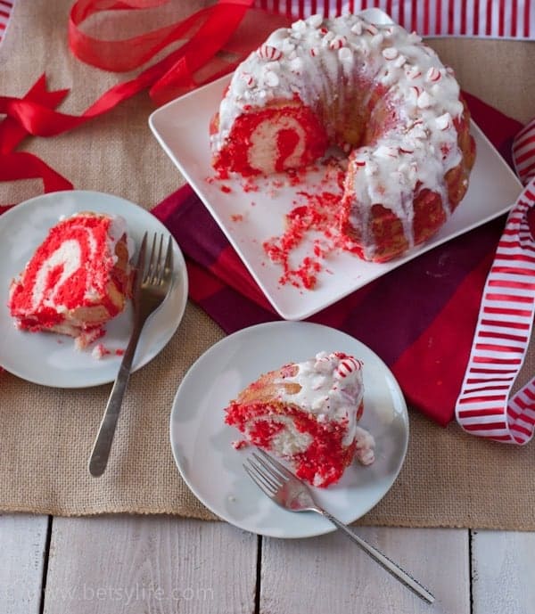 Peppermint Candy Bundt Cake with two slices removed on serving plates with forks. Center of cake is red and white swirled 