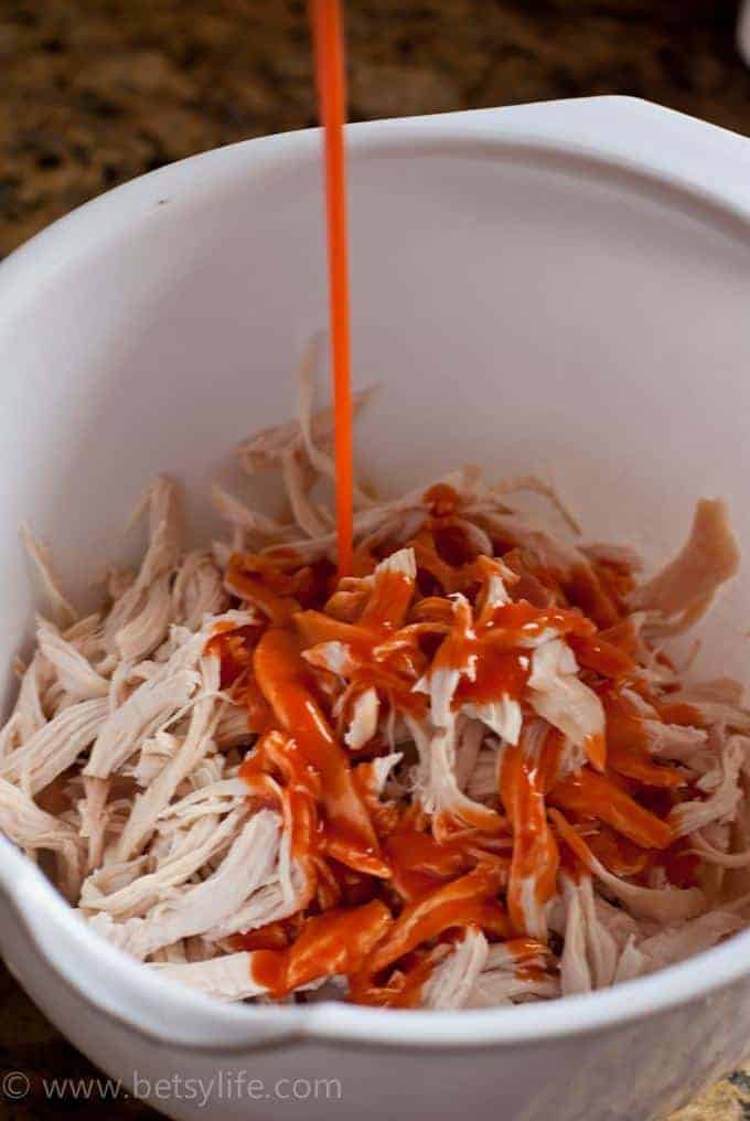 drizzling red sauce on shredded chicken