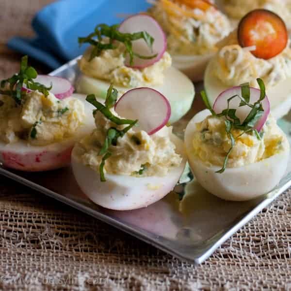 Close up of deviled eggs topped with herbs and radishes on a silver tray 
