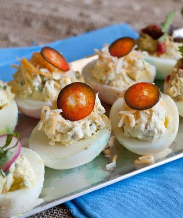Deviled eggs topped with shredded cheese and jalapeno slices on a silver tray 
