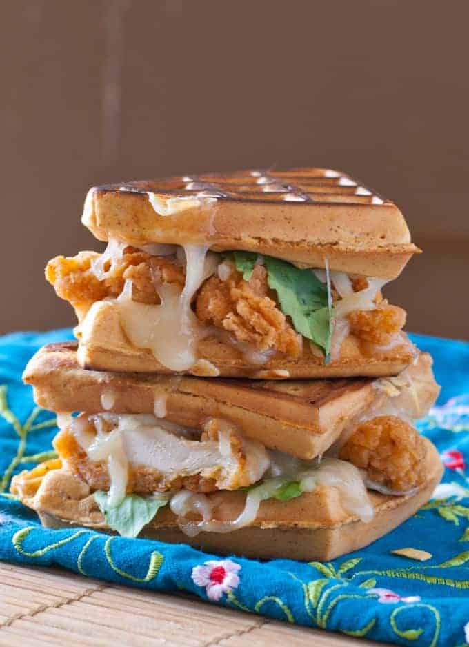 Stack of two waffle sandwiches with fried chicken strips and melted cheese sitting on a blue floral print napkin