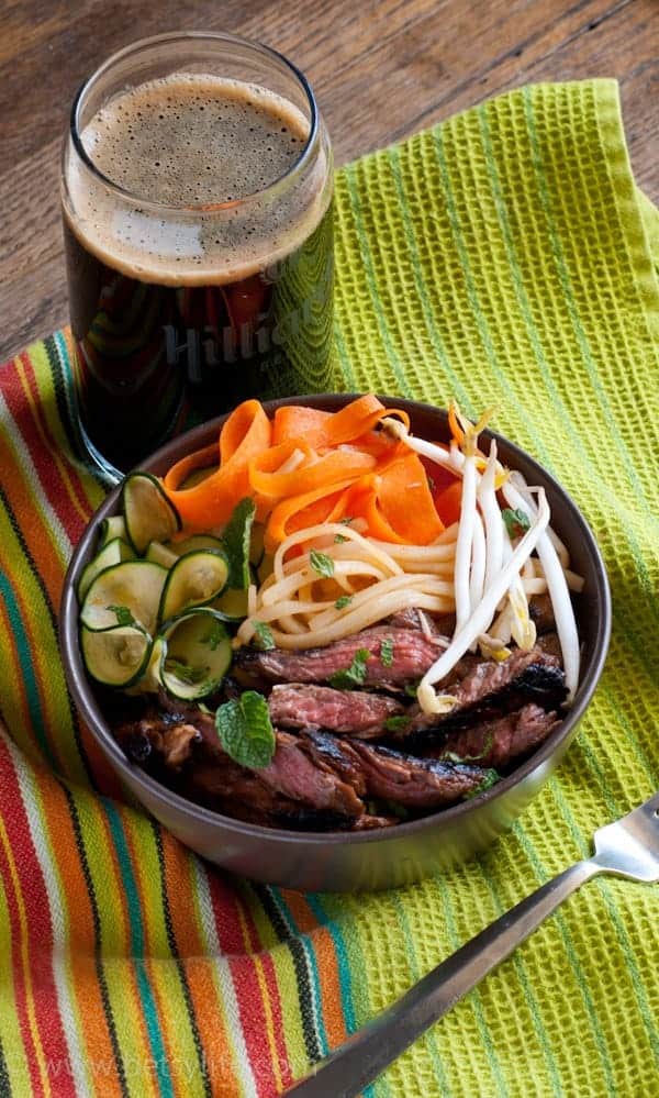 Hoisin Flank Steak Noodle Bowl on a green linen next to a dark beer