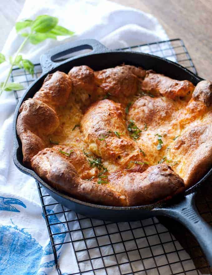 Dutch baby pancake in cast iron skillet with white towel and green herbs