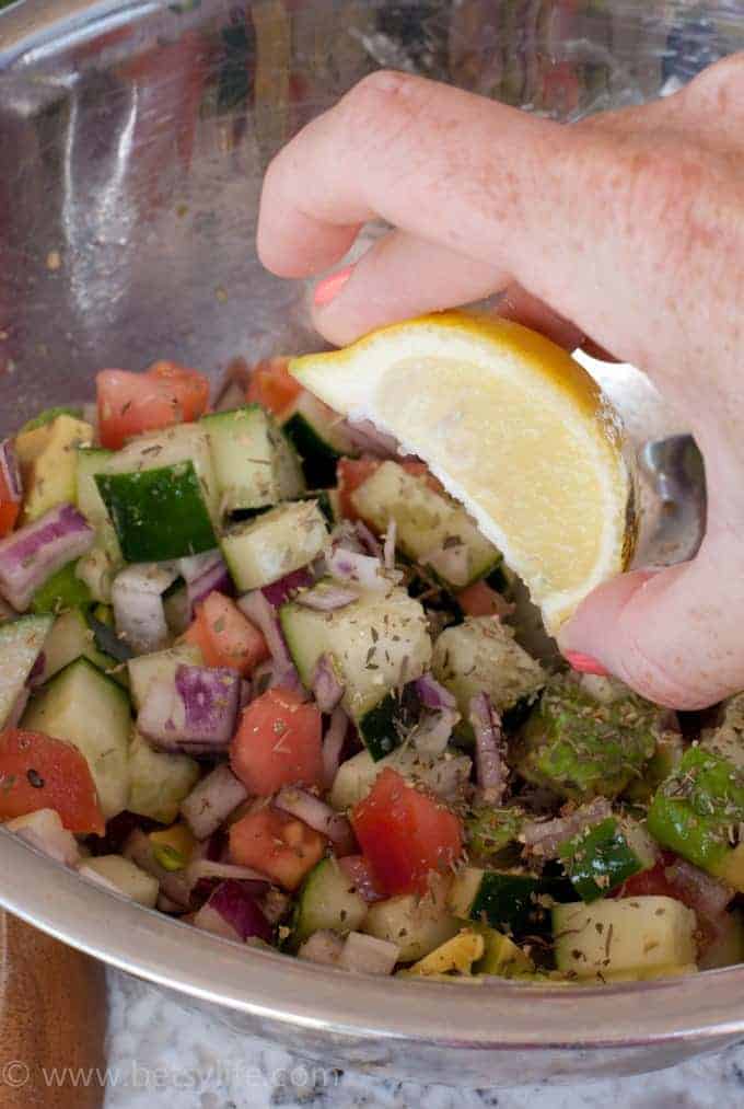 bowl of diced cucumber, onion, and tomato being squeezed with lemon juice