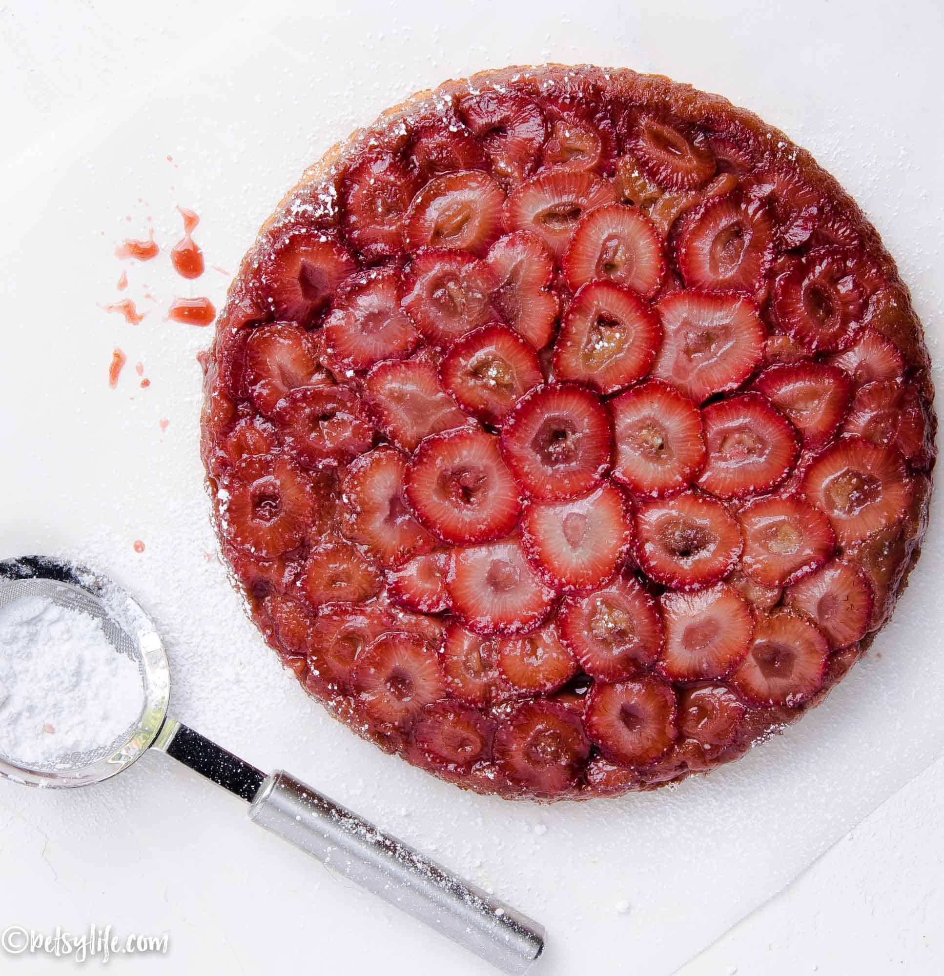 overhead of strawberry upside down cake next to a sifter filled with powdered sugar 