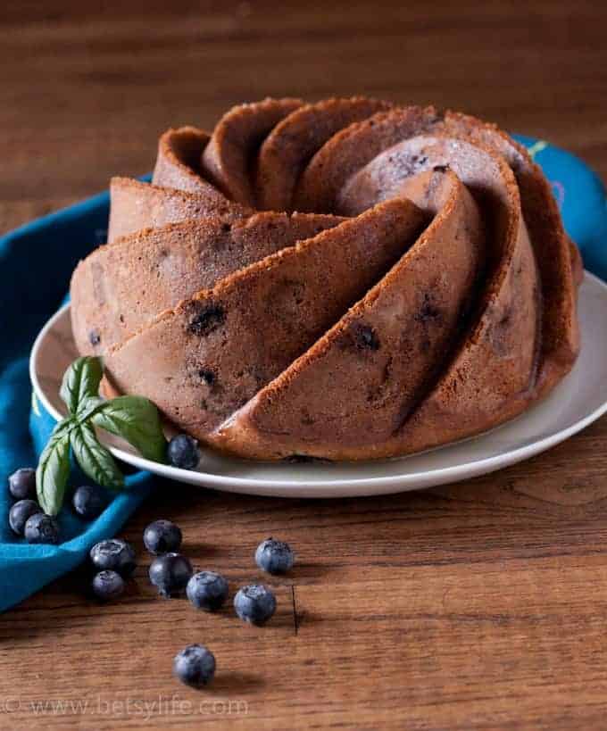 Basil Blueberry bundt cake on a white plate with blueberries and basil leaves scattered in the foreground 