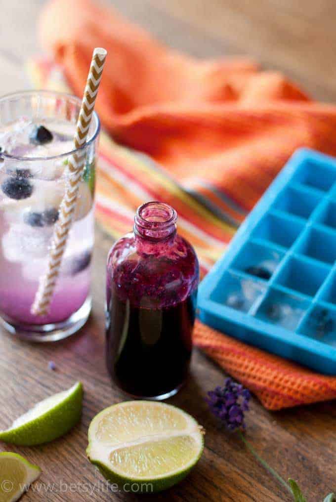 Blueberry Lavender Cocktail in the background. Bottle of blueberry syrup in the foreground. 