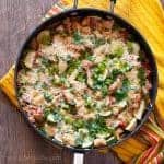 Overhead photo of a large skillet sitting on a yellow towel. Skillet contains spicy one pot chicken and summer vegetable casserole topped with melted cheese and fresh herbs