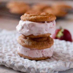 Two Snickerdoodle and Roasted Strawberry Ice Cream Sandwiches stacked with a cooling rack filled with snickerdoodle cookies out of focus in the background