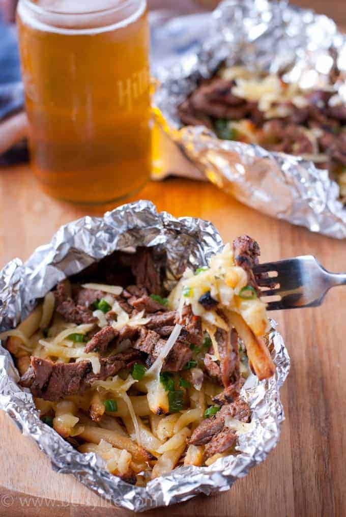 meat and french fries on fork with foil packet and beer