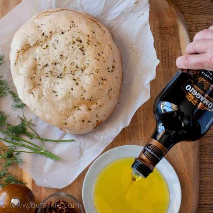 loaf of bread next to a hand pouring olive oil into a bowl 