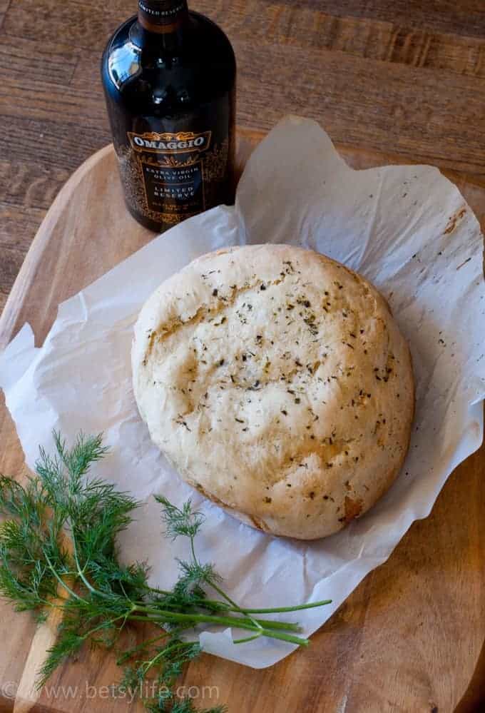 Loaf of Olive Oil & Herb Crock Pot Bread on parchment with fresh dill