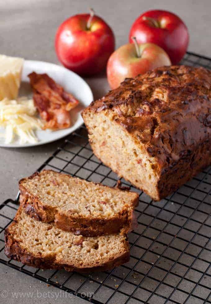 Bacon Apple Cheddar Bread sliced on a cooling rack with apples in the background 