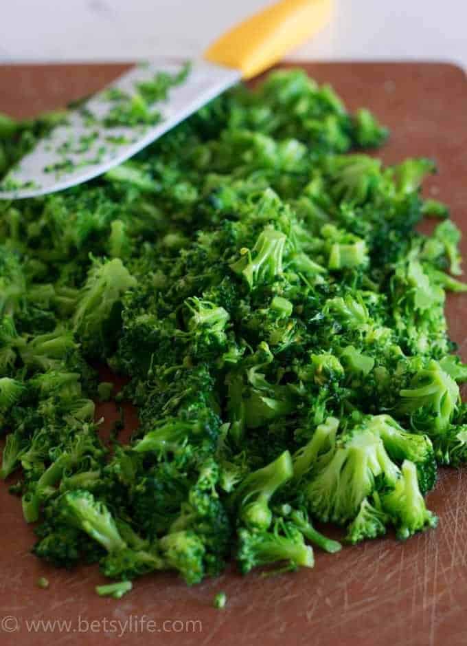 Finely chopped broccoli on a wooden cutting board. Knife with a yellow handle in the background