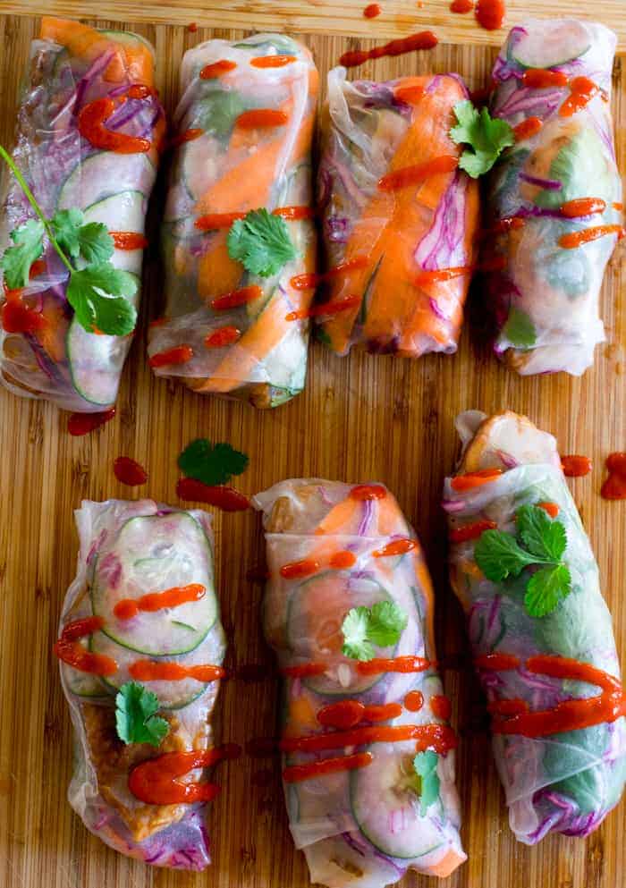 Overhead of 7 fresh spring rolls drizzled with sriracha and topped with cilantro leaves