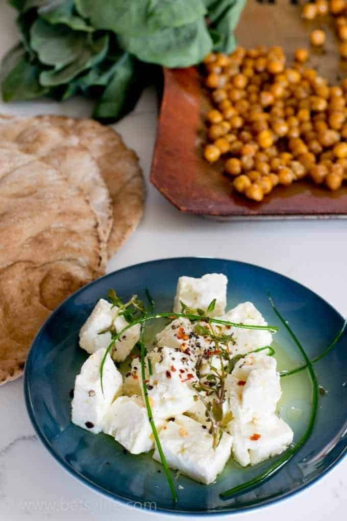 blue plate of marinated feta chunks with a tray of crispy chickpeas in the background 