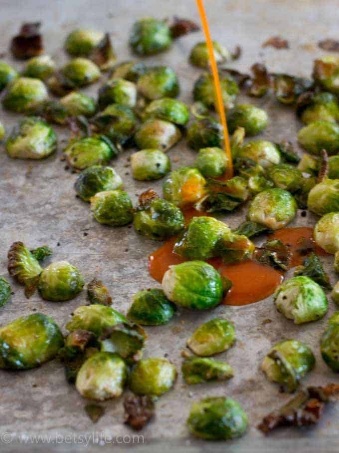 roasted Brussels sprouts on a sheet pan with buffalo sauce being poured over the top 