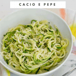 Spiralized zucchini noodle cacio e pepe in a white bowl with a fork in the foreground
