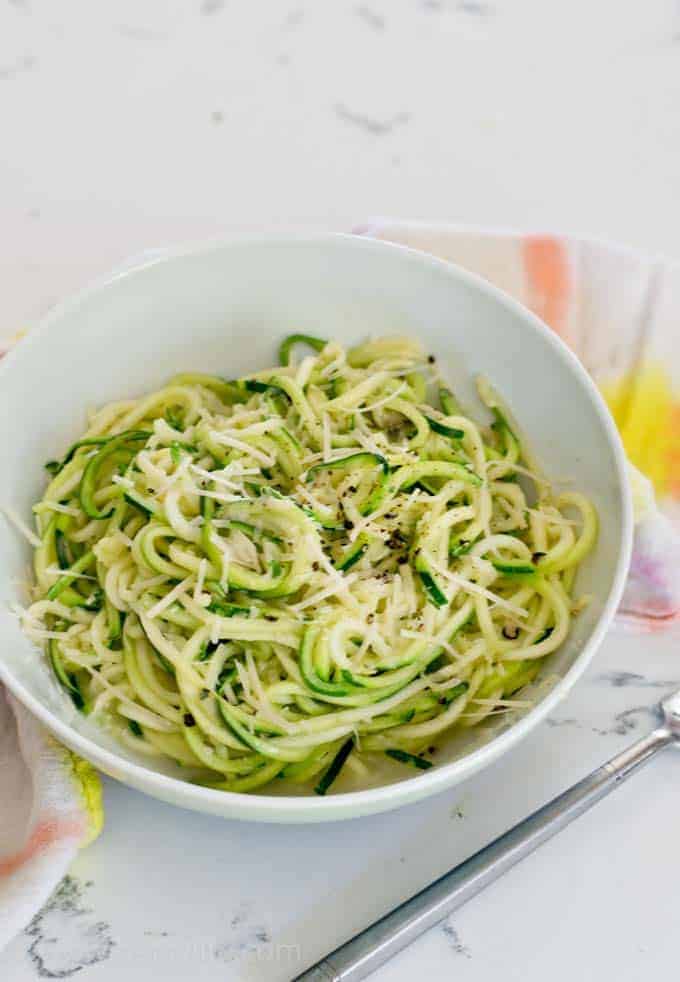 Spiralized zucchini noodle cacio e pepe in a white bowl with a fork in the foreground