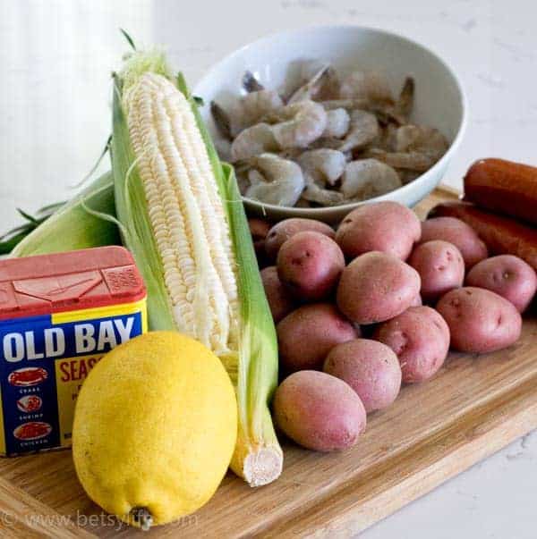potatoes, corn, shrimp, old bay seasoning and a lemon on a cutting board