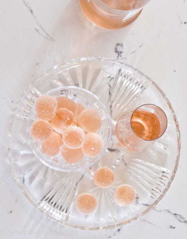 Rosé Wine gummies on a glass plate next to a bottle and a glass of pink wine 
